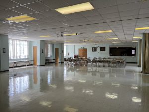 Image depicts Fellowship Hall with mostly open space and some additional chairs/table set-up in background.